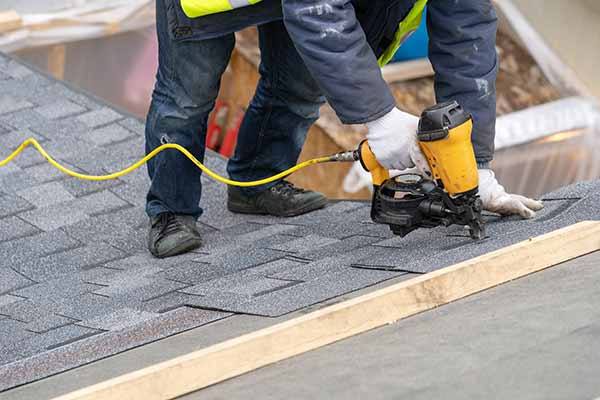 Close up of a worker installing new gray shingles on a residential roof with a nail gun
