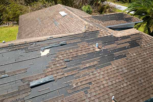 Large residential roof with missing brown shingles due to Hurricane Ian